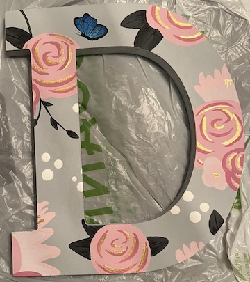 A light grey letter D with painted pink cartoon flowers with gold accents, dark grey leaves, and a blue monarch butterly at the top of the letter
